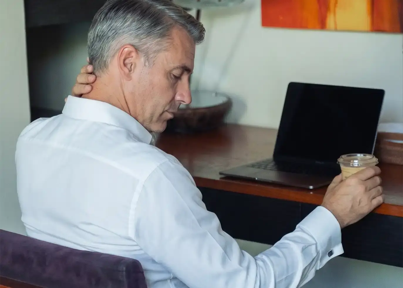 A guest working at a laptop, one hand pressed to the back of his neck
