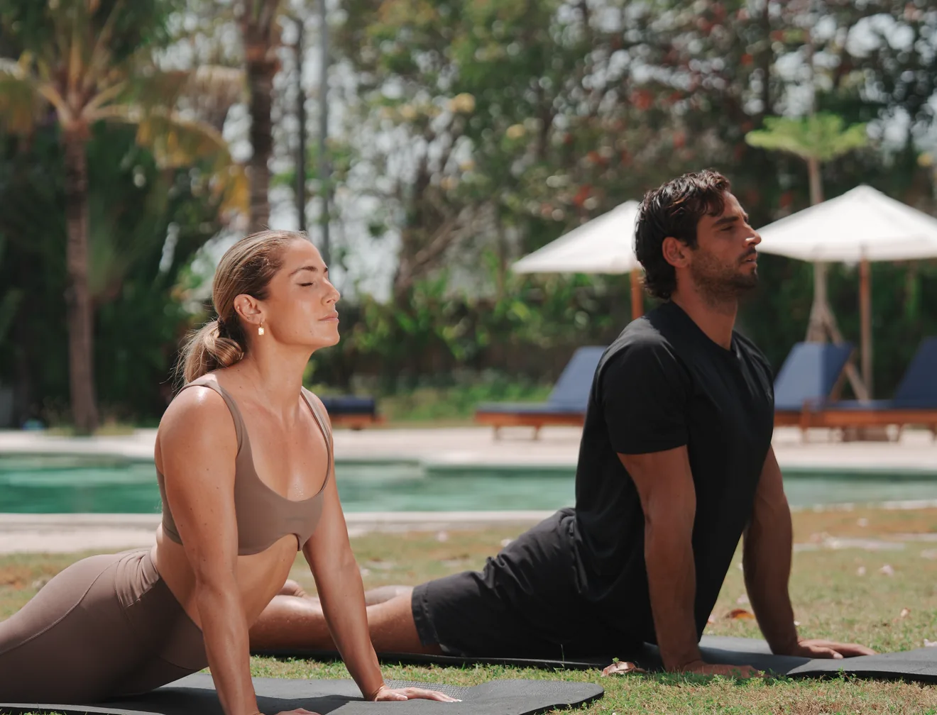 Two guests working through a mobility session on the lawn beside the pool at Pronoia Bali